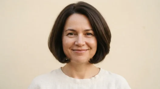 Woman with a round face wearing a curved chin-length bob with ends sitting just at the jaw, warm cream backdrop