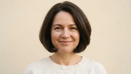 Woman with a round face wearing a curved chin-length bob with ends sitting just at the jaw, warm cream backdrop