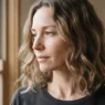 Woman with air-dried fine wavy collarbone-length hair beside a tall window with soft natural daylight across the hair surface