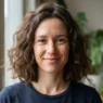 Woman with wavy frizzy hair in a blunt collarbone bob, soft window light on a humid day
