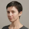 Woman with freshly cut long pixie haircut, hair lightly misted and damp, ready for hand styling, plain neutral background