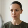 Woman with oval face looking into mirror with hair pulled back, checking face shape in bright room with soft daylight