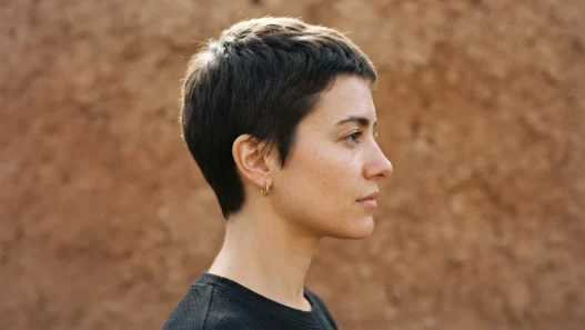 Woman with short cropped haircut in side profile against plain clay backdrop with clean outline lighting