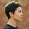 Woman with short cropped haircut in side profile against plain clay backdrop with clean outline lighting