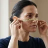 Woman with square jaw measuring cheekbone width with flexible tape measure in natural window light