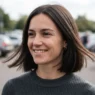 Woman with strong-perimeter bob in open car park with wind lifting the ends at jaw level