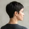 Back and side view of woman with tapered pixie cut showing clean nape taper under hard side light