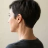 Back and side view of woman with tapered pixie showing clean nape taper and defined perimeter against pale backdrop