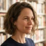 Woman with a textured bob seven weeks grown out, sitting beside a bookshelf in warm afternoon light, hair filling most of the frame