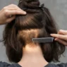 Woman parting thick shoulder-length hair with a tail comb to reveal four dense interior bulk zones in directional lighting