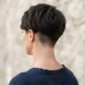 Woman with freshly cut undercut pixie showing razor-clean shaved nape against pale stone wall in open shade