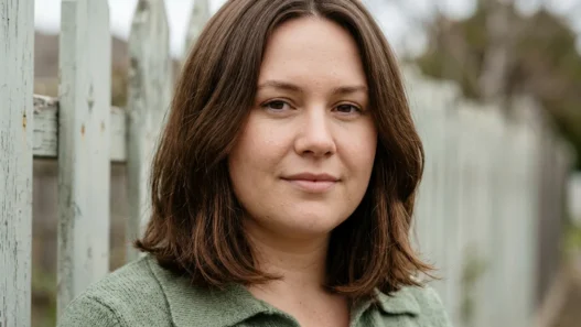 Woman with round face wearing medium collarbone lob with low fullness beside timber fence