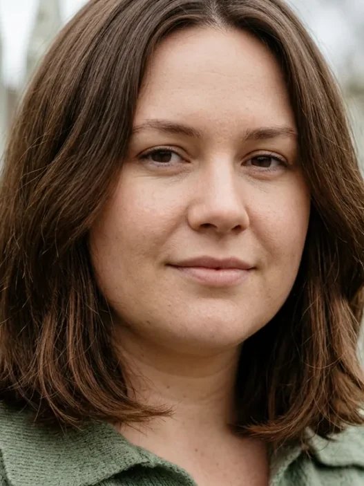 Woman with round face wearing medium collarbone lob with low fullness beside timber fence