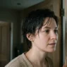 Woman with damp mid-length grown-out pixie standing in doorway landing in cool daylight