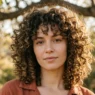 Woman with medium voluminous rounded curly layers under dappled tree light