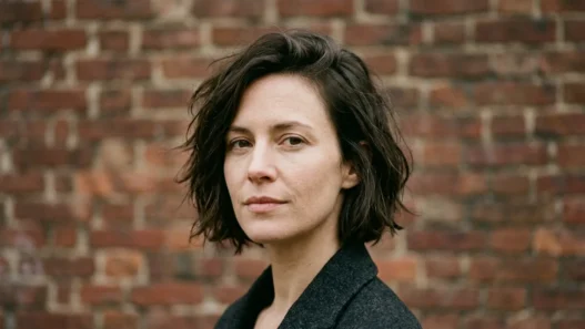 Woman with tousled chin-length bob in three-quarter view against brick wall in daylight