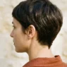 Woman with dark chestnut tapered pixie showing clean nape shape against stone wall